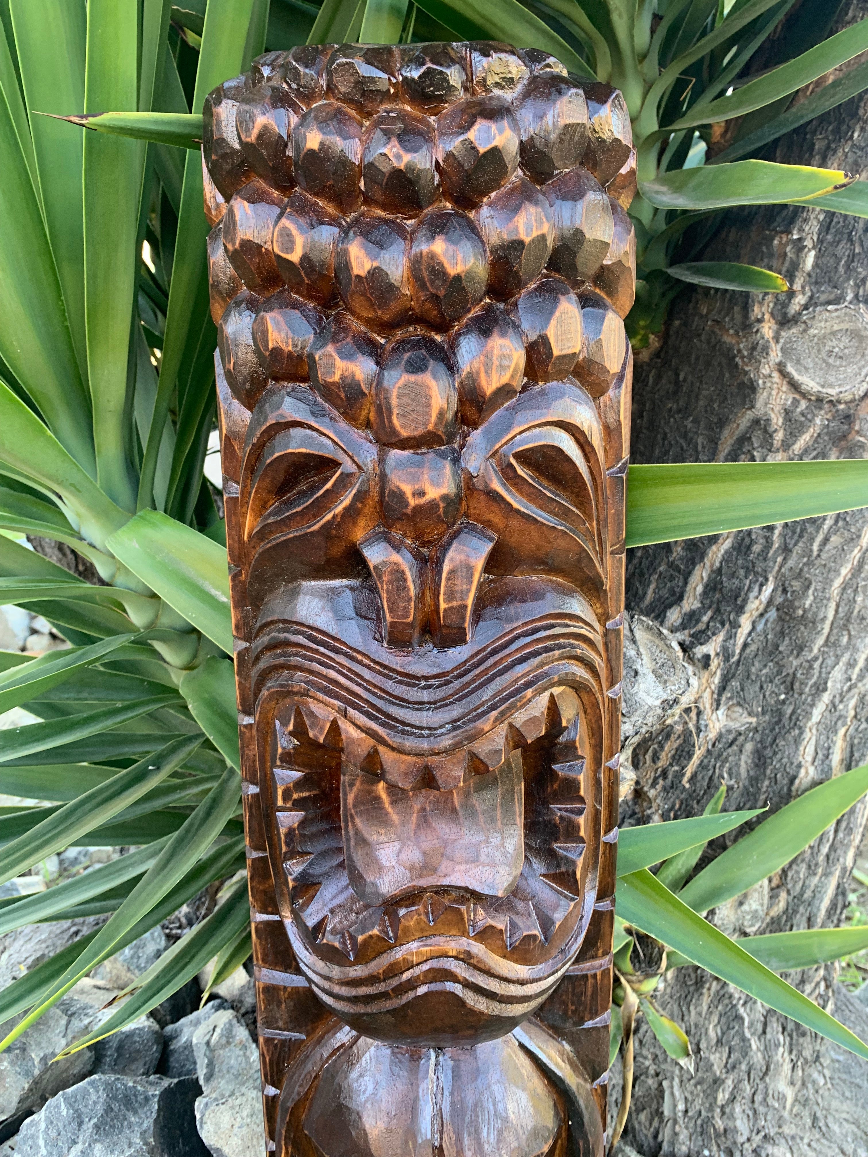 Carved wooden tiki mask with open mouth among tropical plants