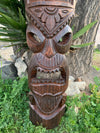 Carved wooden tiki mask sculpture outdoors beside a tree