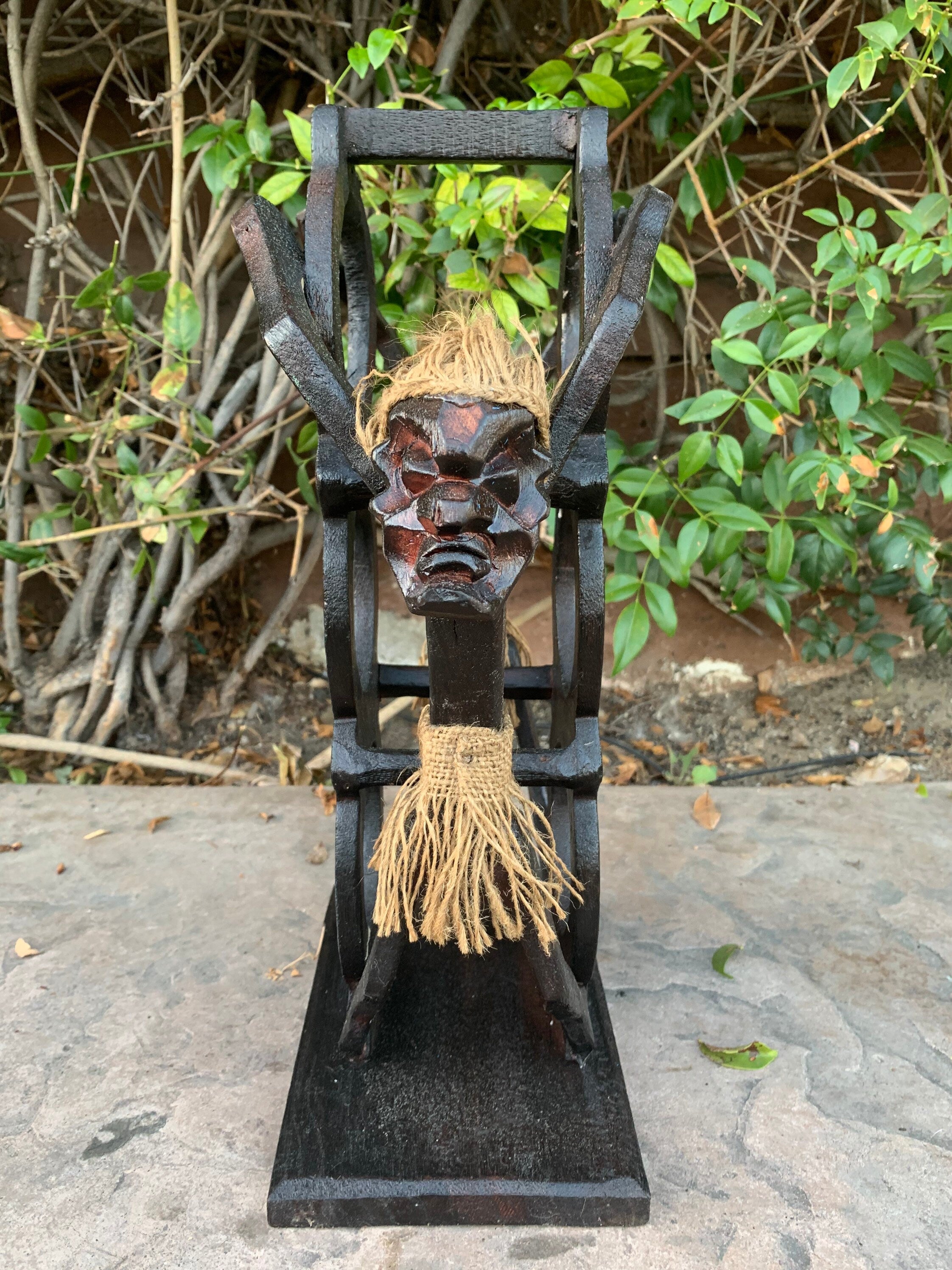 Wooden tiki mask with rope hair mounted on a black wooden frame outdoors
