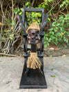 Wooden tiki mask with rope hair mounted on a black wooden frame outdoors
