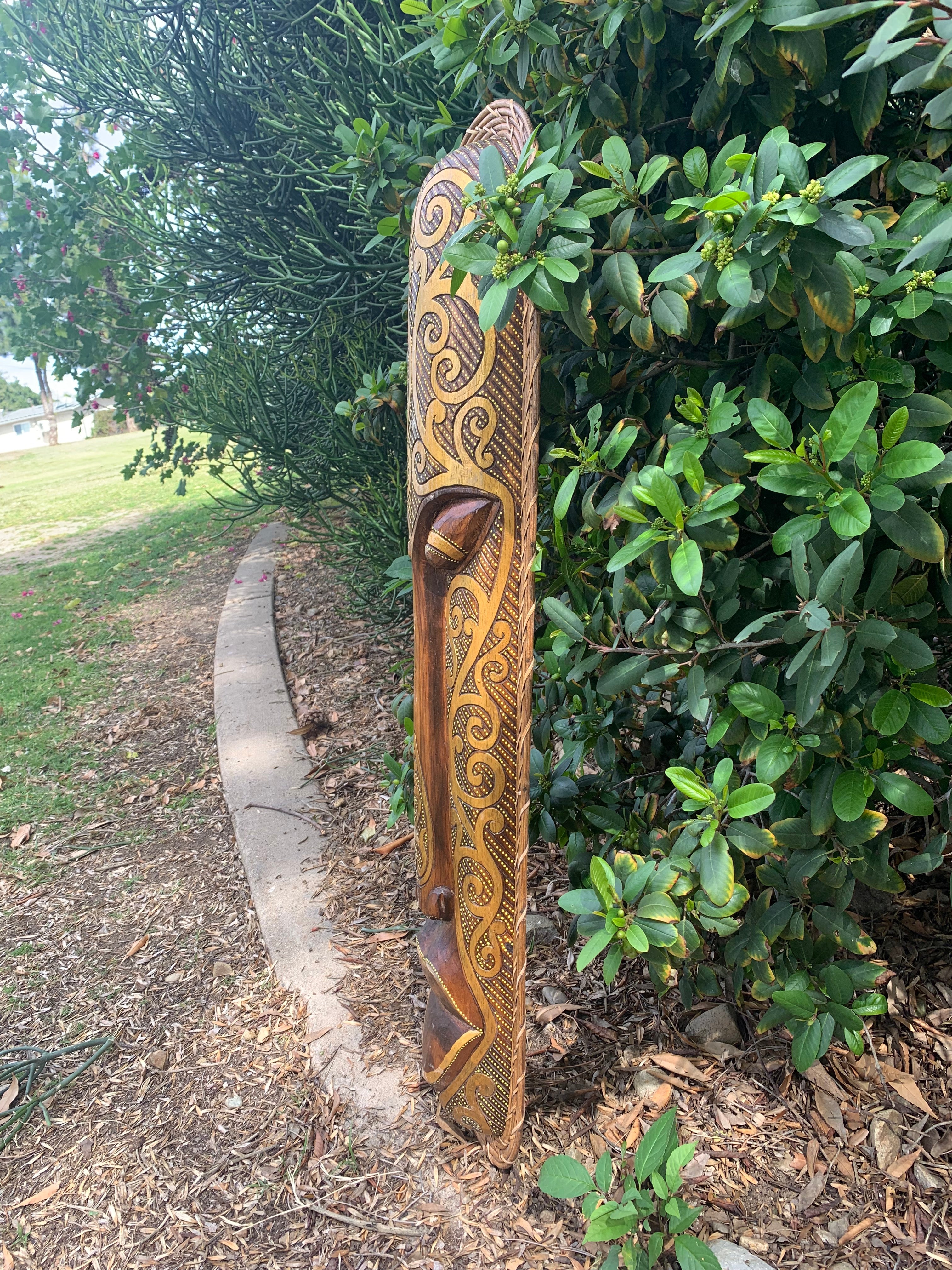 Polynesian tiki carving on a tall wooden pole outdoors among green shrubs