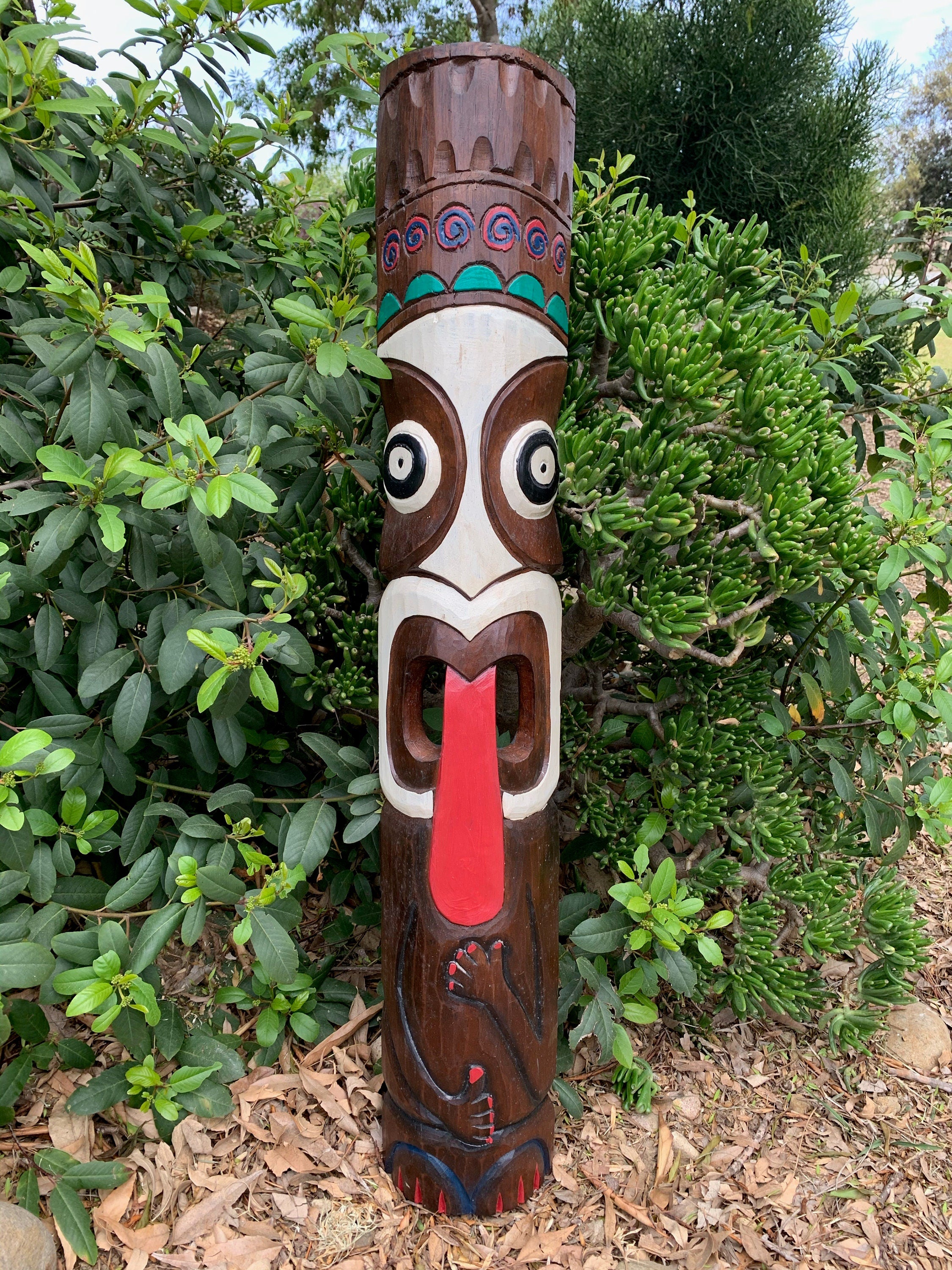 Carved wooden tiki statue in a garden with large eyes and red tongue