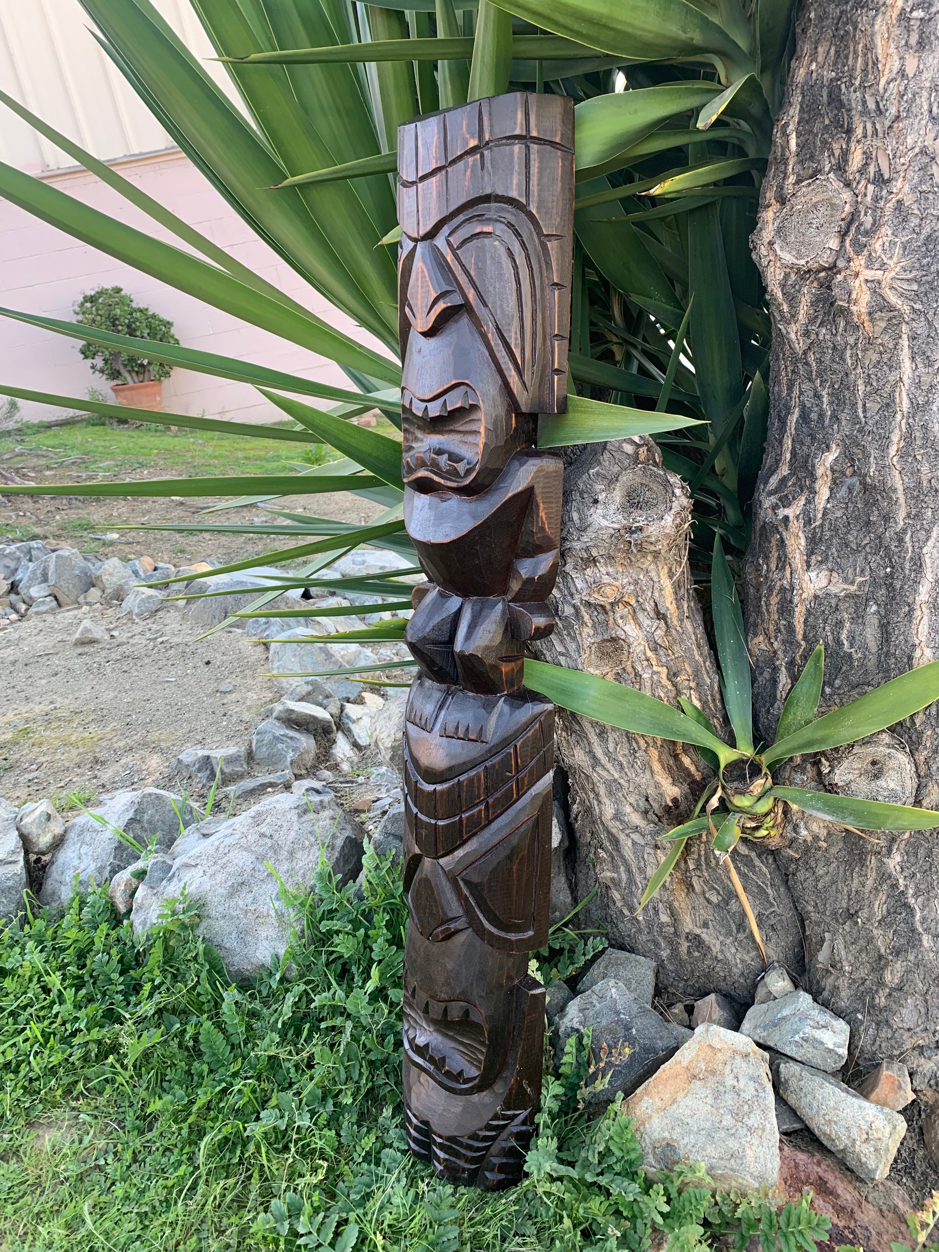 Wooden tiki totem pole carving leaning against a tree in a garden