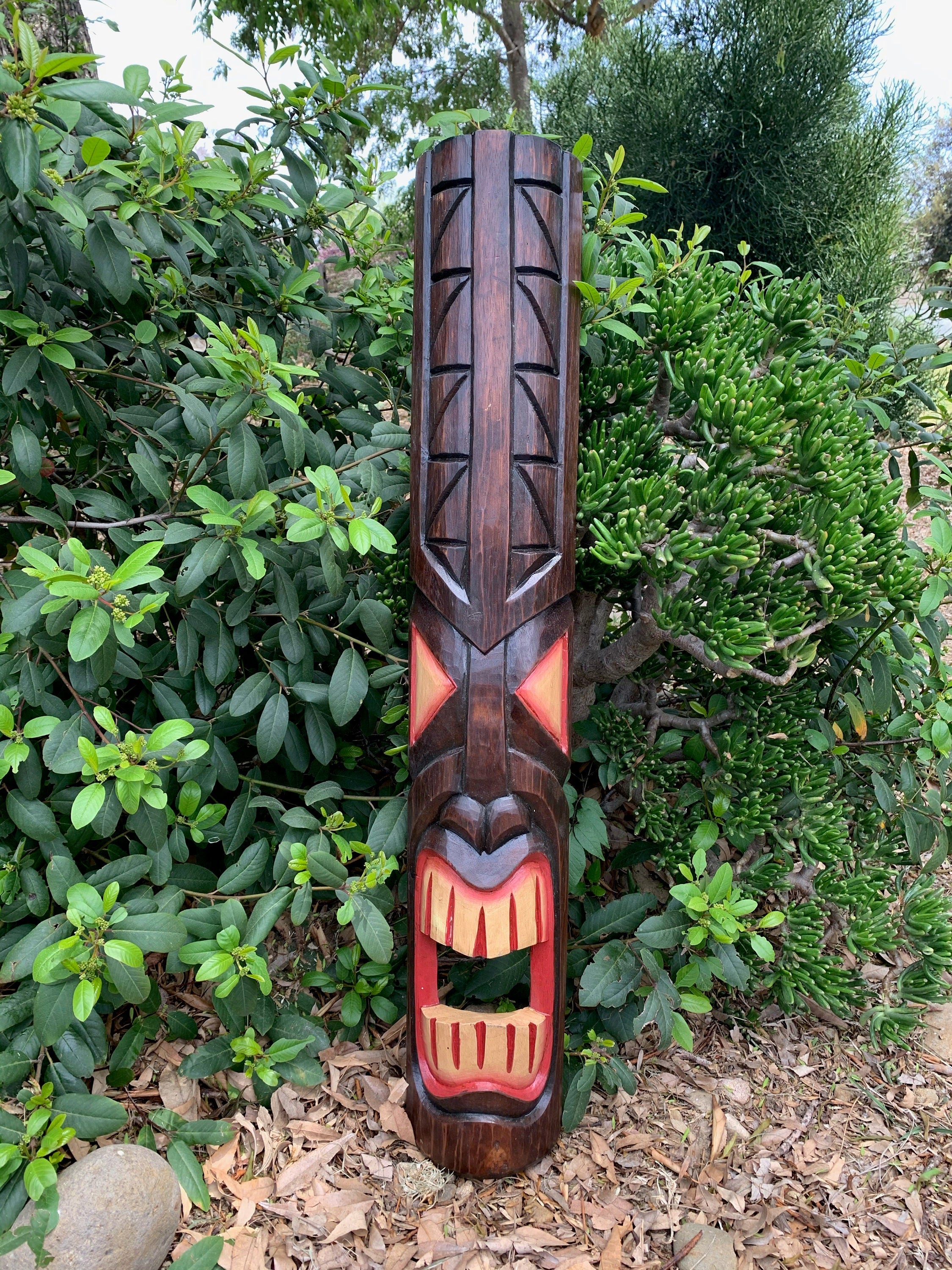 wooden tiki totem statue carved with a wide open mouth in a garden setting