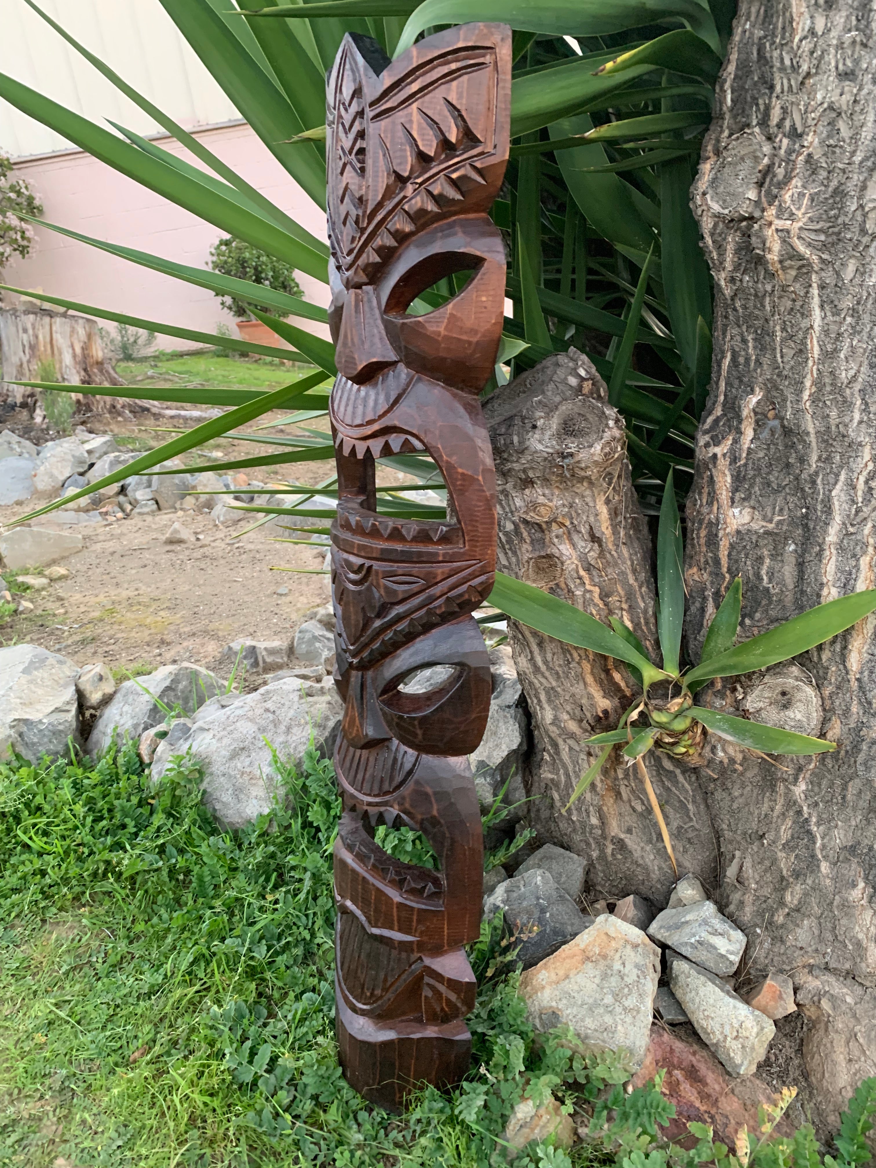 Wooden carved totem pole with geometric faces in a garden beside a tree