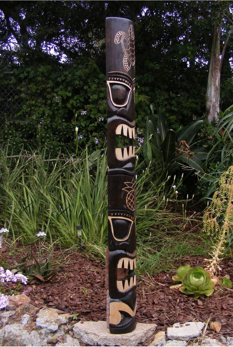 carved wooden totem pole in a garden setting with plants and mulch