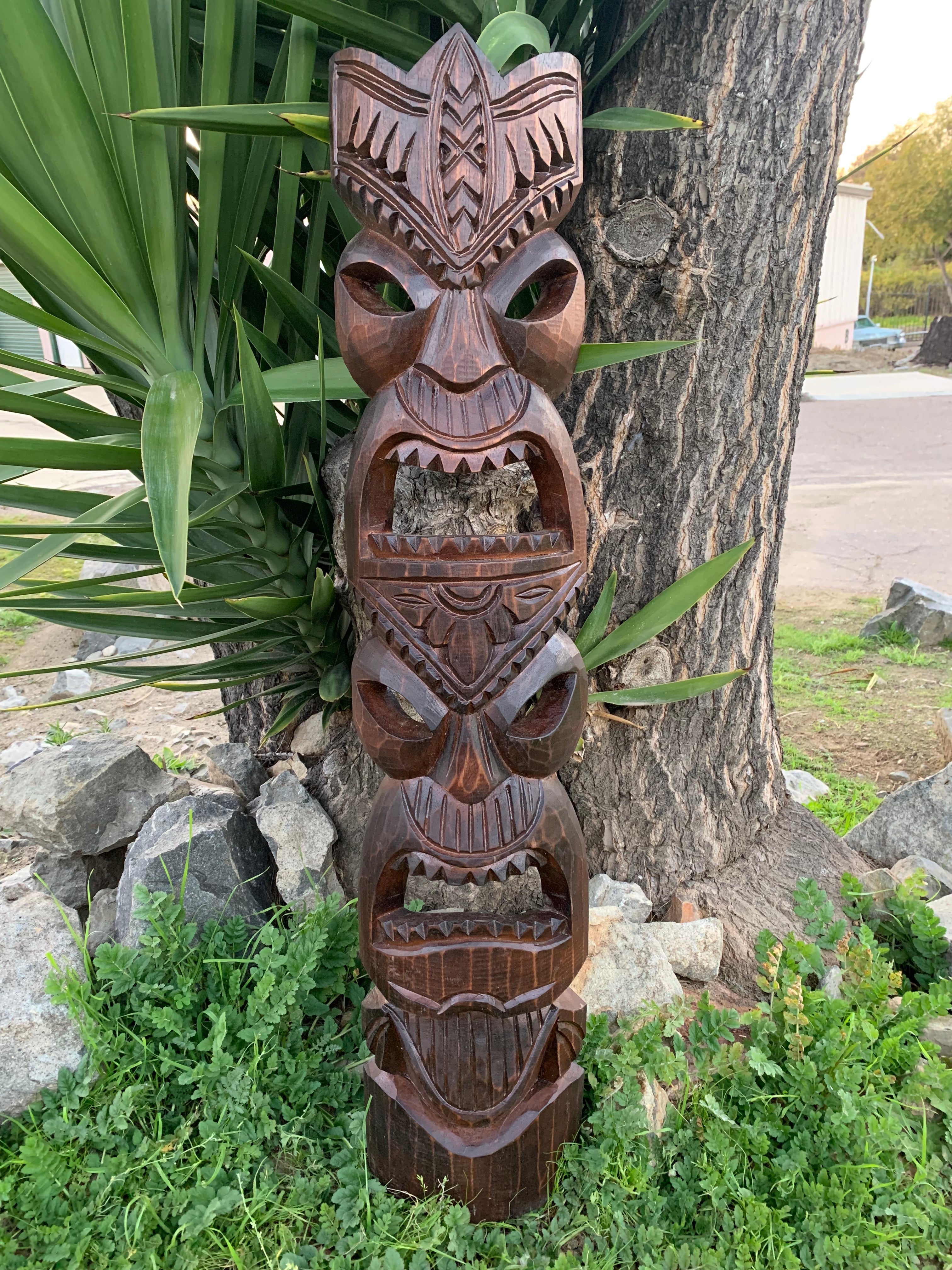 Stacked carved wooden totem pole with multiple faces beside a tree in a garden