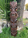 Stacked carved wooden totem pole with multiple faces beside a tree in a garden
